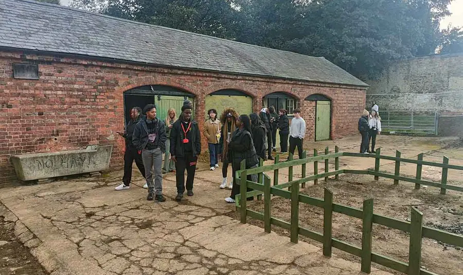 A group of young people stand in front of a red brick stable block