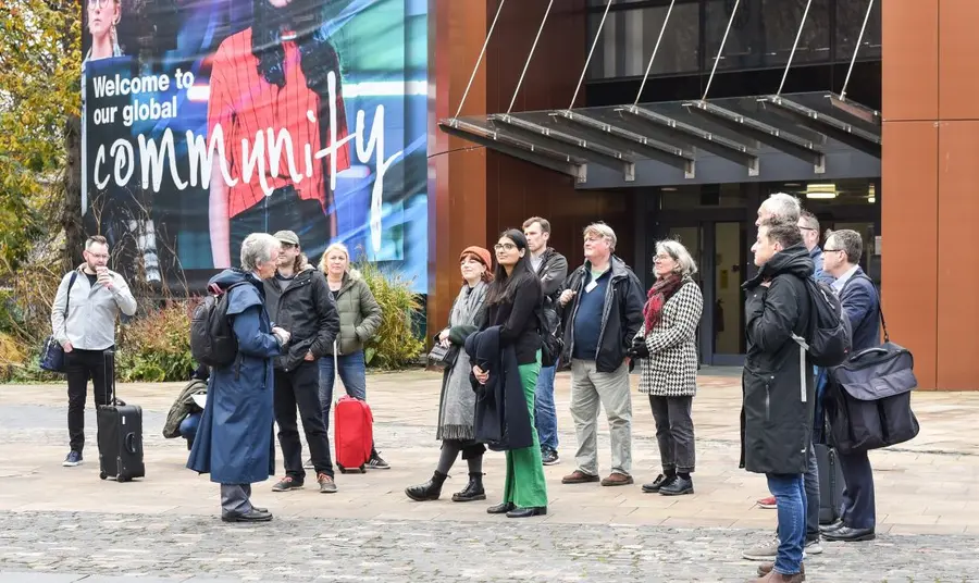 A group of 13 people standing outside a building listening to a tour guide as part of a community walking tour