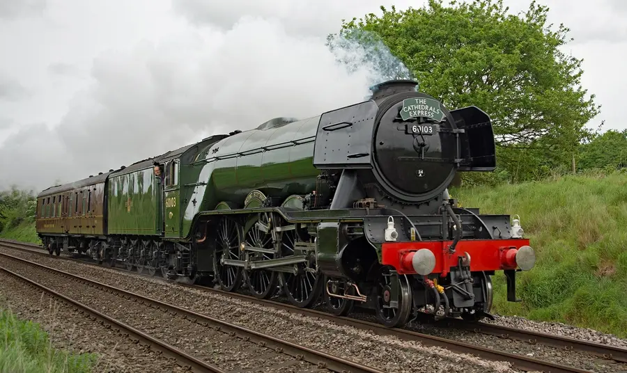 The Flying Scotsman, a large dark green steam engine, pulls a heritage service through the countryside.