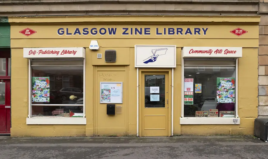 A yellow building on a city street with a writing saying Glasgow Zine Library