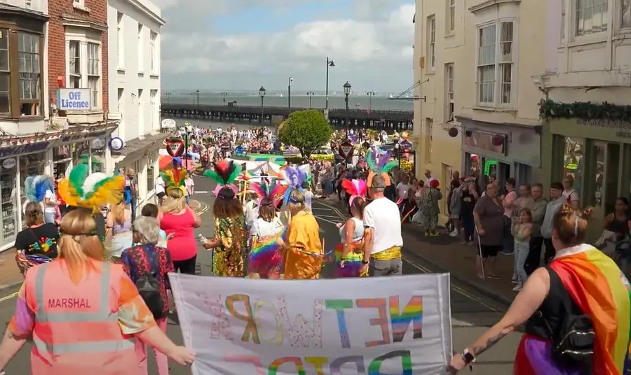 People wear colourful clothes and hold banners and rainbow flags at Isle of Wight Pride.