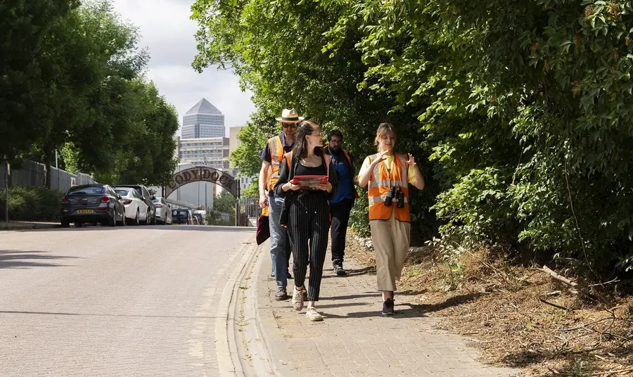 People with high visibility jackets, clipboards and binoculars walking within an urban nature spot in Newham, London