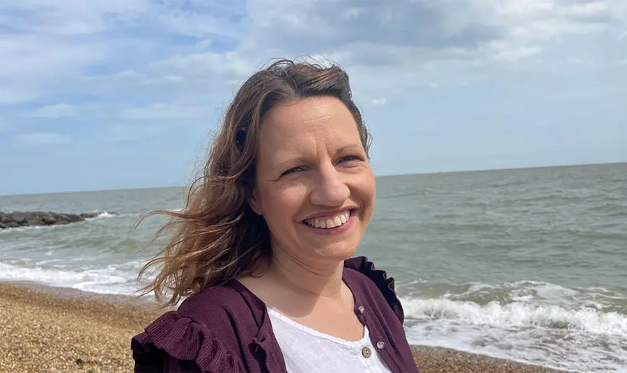 A woman with light brown hair and white skin stands on a beach