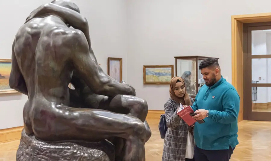 A couple looking at a map in a museum while standing in front of a sculpture
