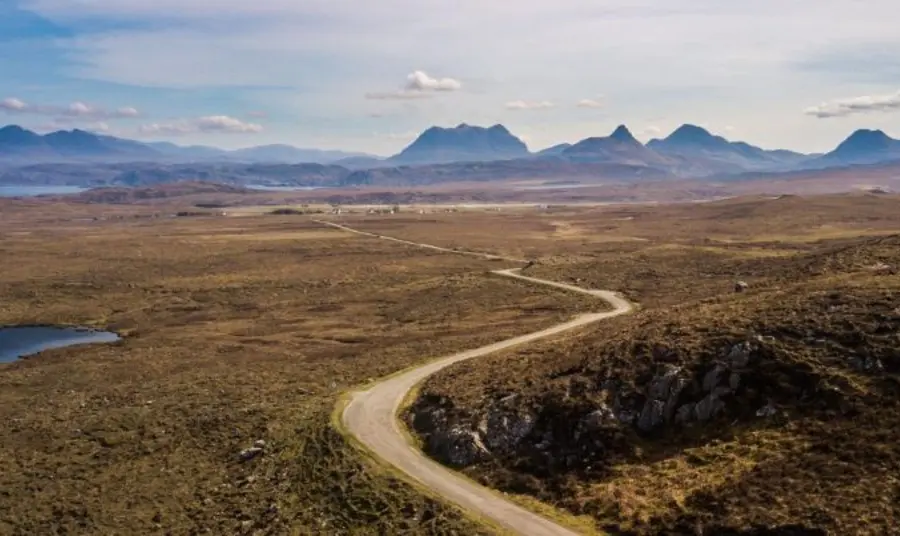 A vast landscape view with a path in the foreground leading into the distance, and mountains along the horizon