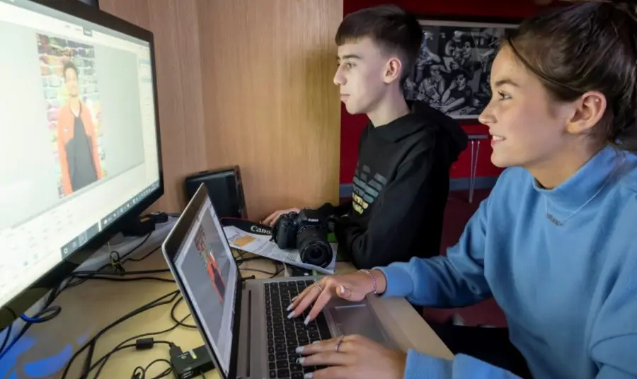 Two young adults sitting in front of multiple computer screens as they edit a video