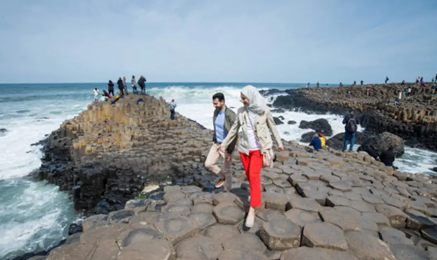 An Asian couple in the foreground, with other visitors in the background, exploring the Giant's Causeway