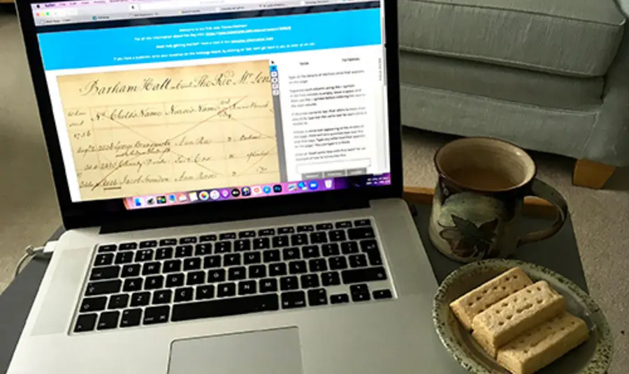 A laptop screen which shows an old letter on it. Next to the laptop are four pieces of shortbread.