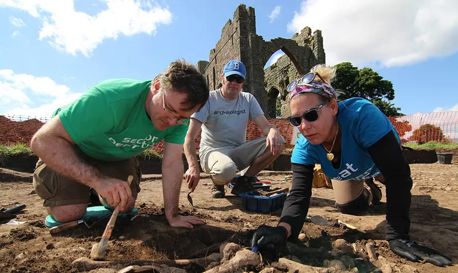 Three people use trowels and brushes to excavate around bones in an archeological dig