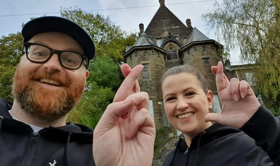 A Two people standingin front of a heritage site doing the crossed fingers selfie