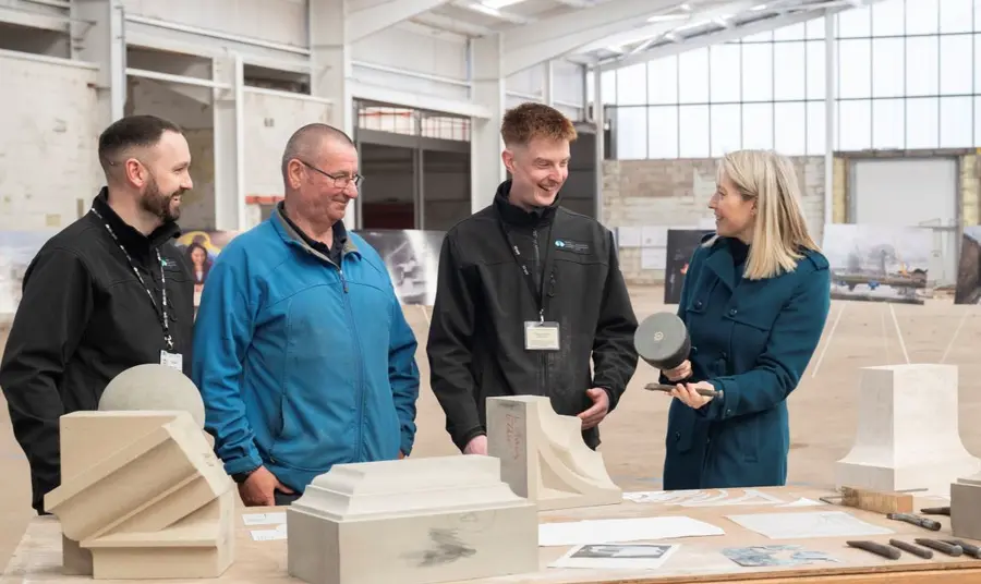Three stonemasons talk to a member of the Heritage Fund team about a selection of tools and craft items from their workshop.