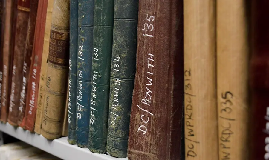 A bookshelf of old books in an archive. The books have reference numbers written on their spines.