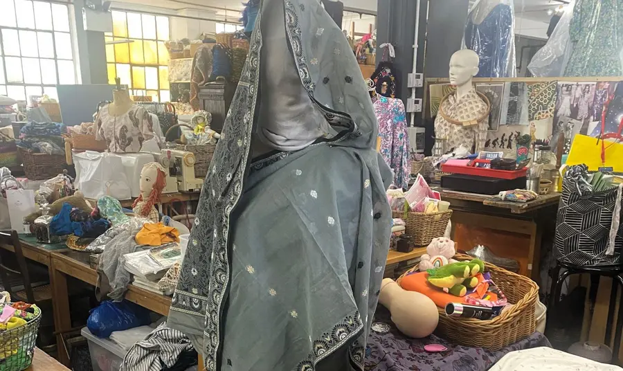 A mannequin with a Sari draped around is standing in a textile workspace