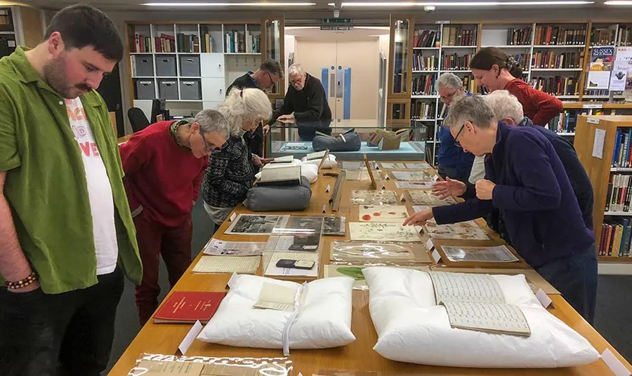 a group of people look at objects from a historical archive laid out on a long table