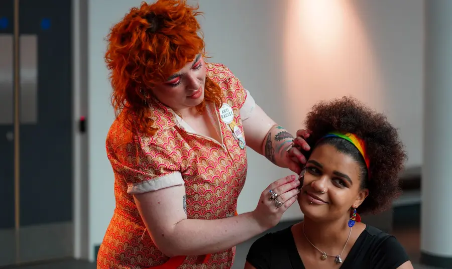 Two people preparing for a party. One person is having a temporary transfer applied to their face. 
