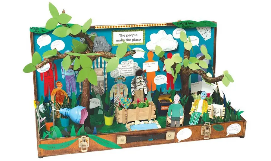a memory box made during a craft activity at a mental health community centre: inside an old case is a garden scene with trees, planters and a pond, with figures and messages