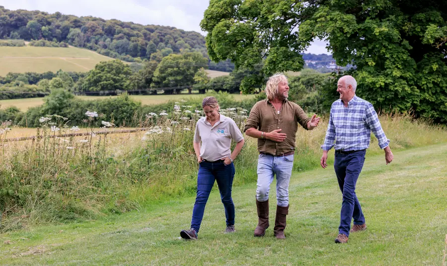 Three people are walking side by side in a pretty green landscape, they are talking and smiling