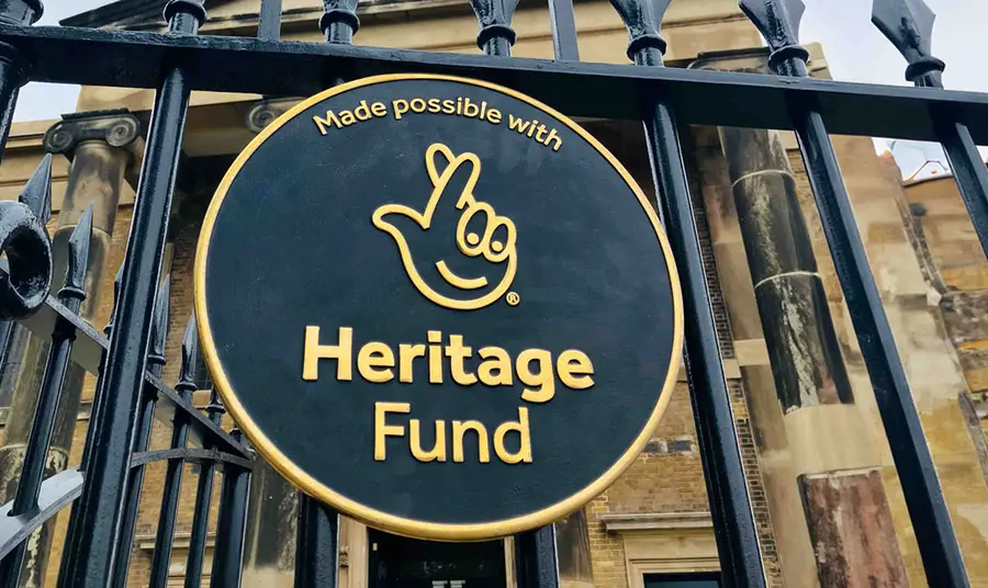 A round plaque of our acknowledgment stamp affixed to an iron fence. A building can be seen in the background.