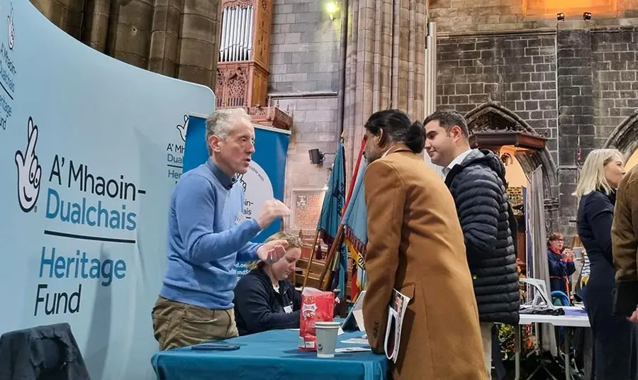 A Heritage Fund member of staff talks with two people at a stall inside a large church