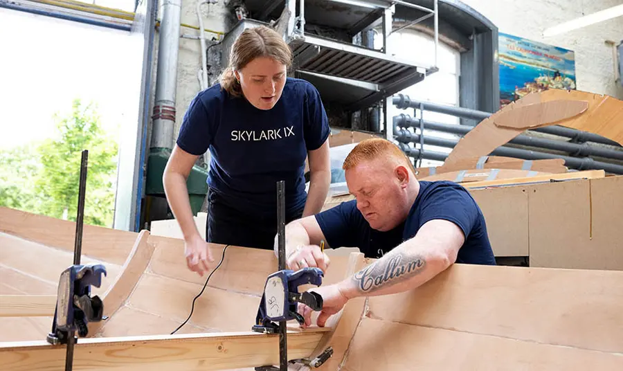 Two Skylark IX volunteers work on building a wooden rowing boat 
