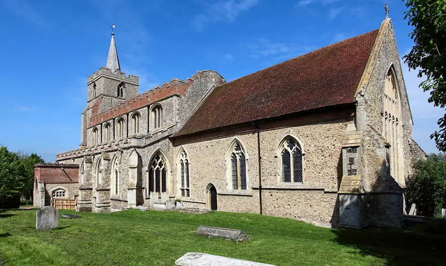The outside of a stone English parish church with a graveyard in the foreground