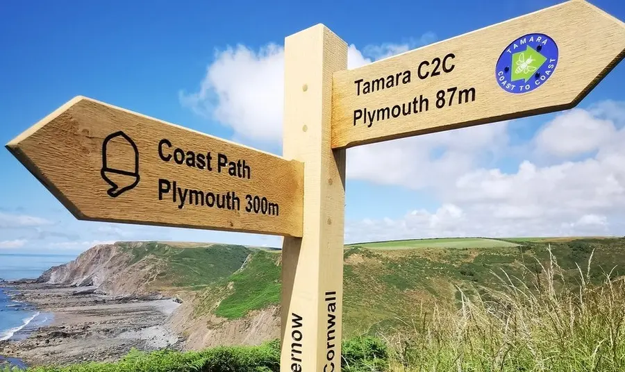 A wooden signpost pointing one way to Plymouth 300 miles away, and another way to the Tamara Coast to Coast route with Plymouth 87 miles away.