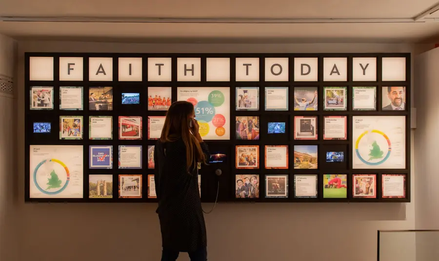 A visitor listens through an exhibition headset in front of a display of information about faith