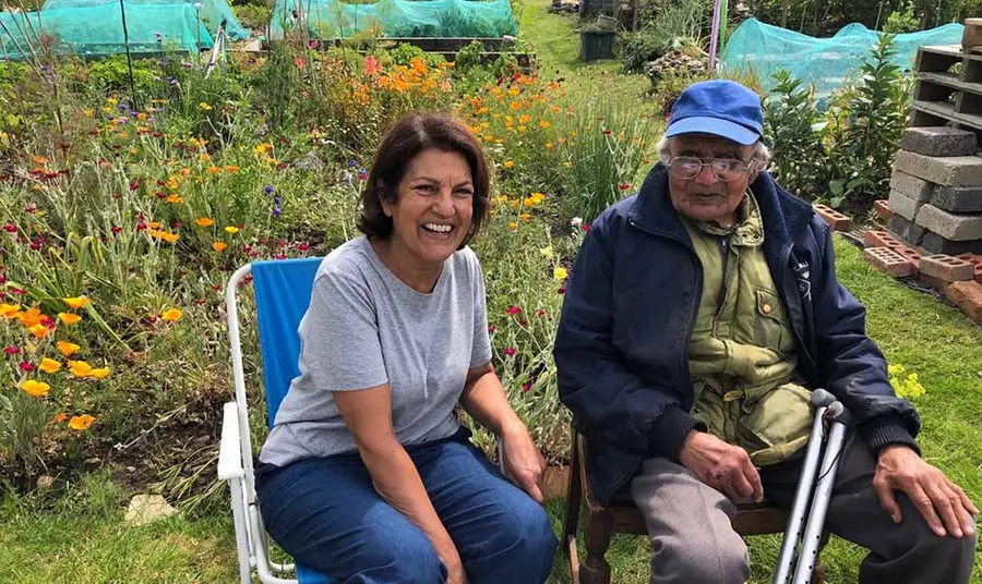 Two people smiling and sitting in camping chairs on an allotment