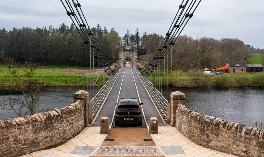 A car crosses the Union Chain Bridge, a small restored suspension bridge over a river.