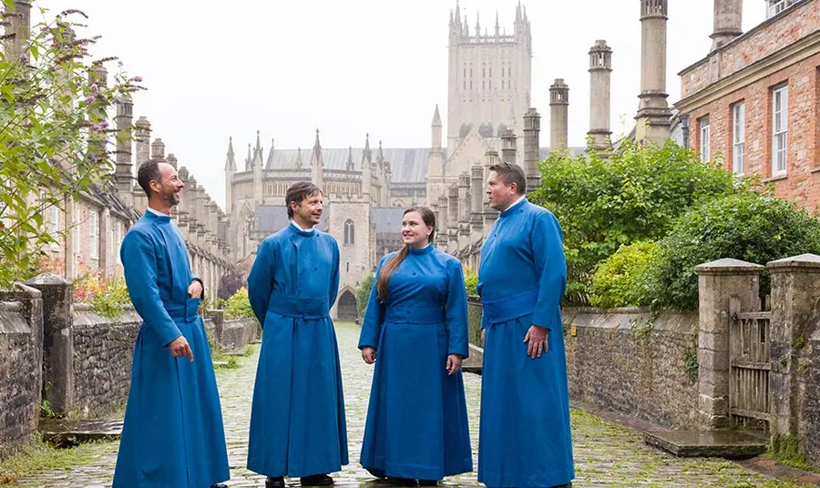 Members of Wells Cathedral’s Vicars’ Choral wear long blue robes and stand outside their medieval stone and brick homes on Vicars’ Close in Wells