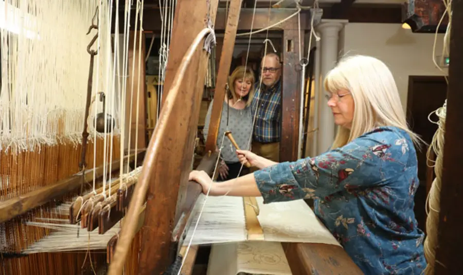 Irish linen damask handloom A person weaves cream coloured fabric on a wooden handloom