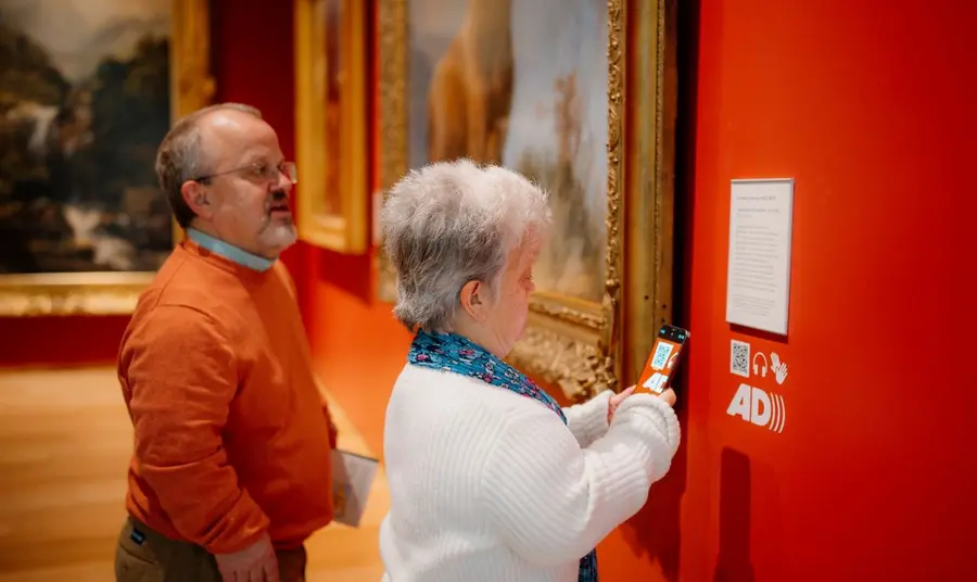 Visitors access audio guides and further resources with their smartphone. Two visitors use a smart phone to scan a QR code that unlocks additional interpretation and audio guides about the Scottish national collection.
