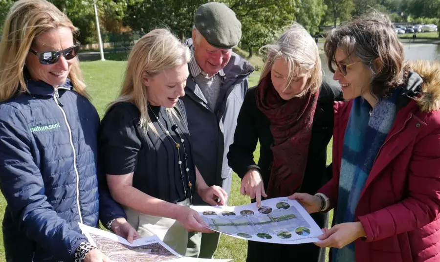Five people in a park looking at plans on A3 size paper