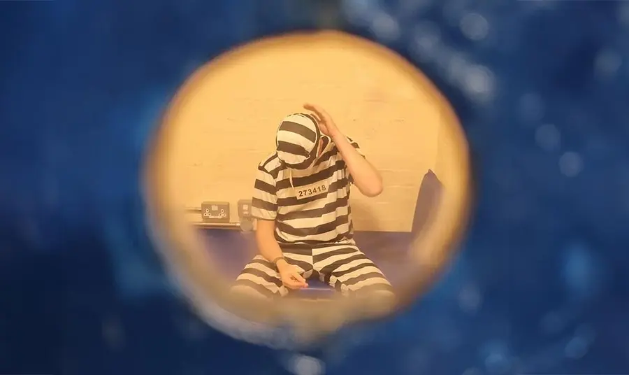 A photo taken through a keyhole of a prisoner in a cell, wearing striped black and white clothing.