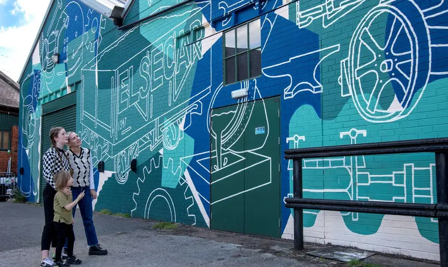 Three people standing in front of a wall painted with a mural in green and blue colours