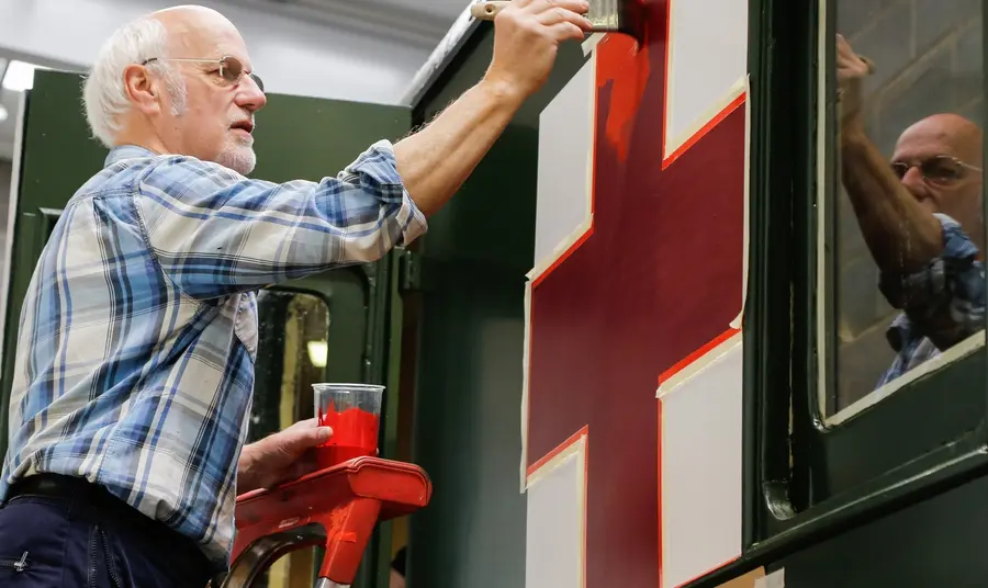 Expert painter Adrian Ashby carefully applies a red cross emblem to the side of a 1907 railway carriage