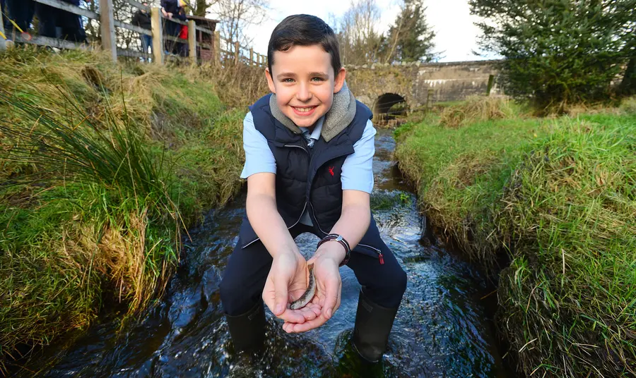 A boy holds a fish in the Ballinderry River
