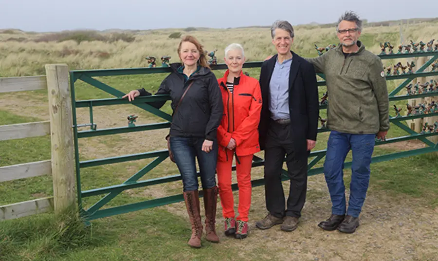 Four people stand in front of a fence