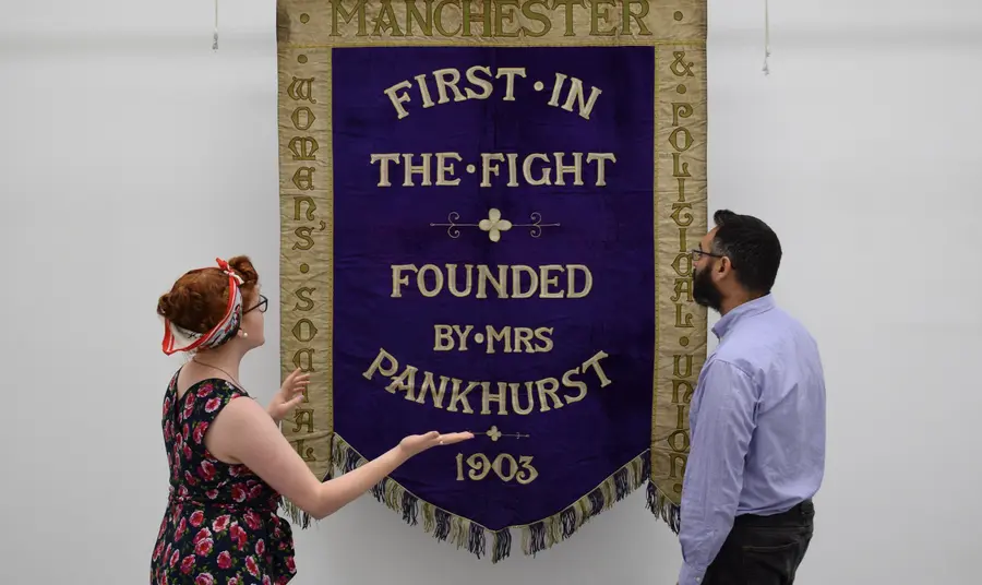 Celebrating the local voices of Women’s Suffrage Helen Antrobus & Adam Jaffer from the People's History Museum with the Manchester suffragette banner