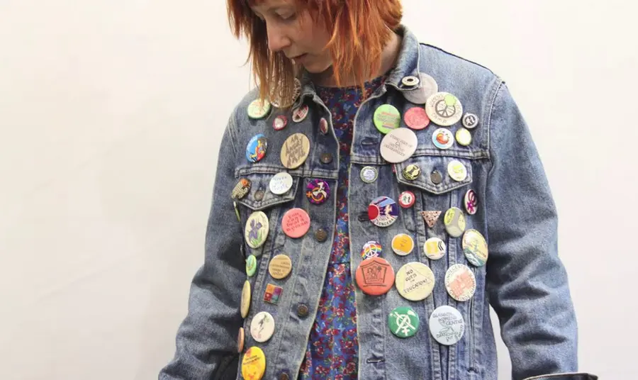A young woman wearing a denim jacket covered in badges