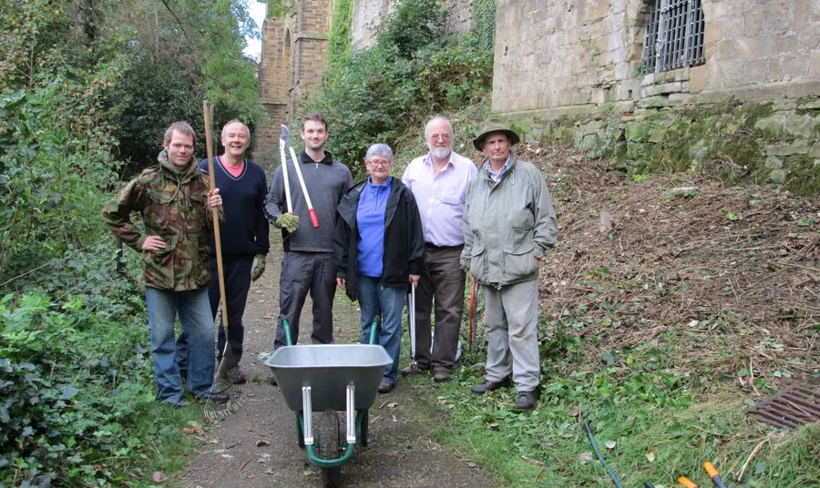 A group of volunteers with gardening tools stand by the cathedral walls