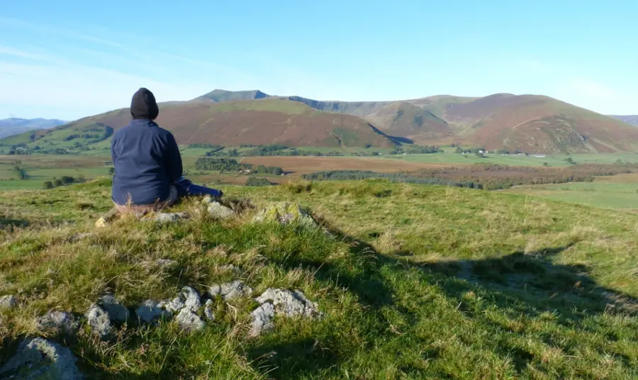 A person sitting on a rock looking towards a hill called Blencathra 