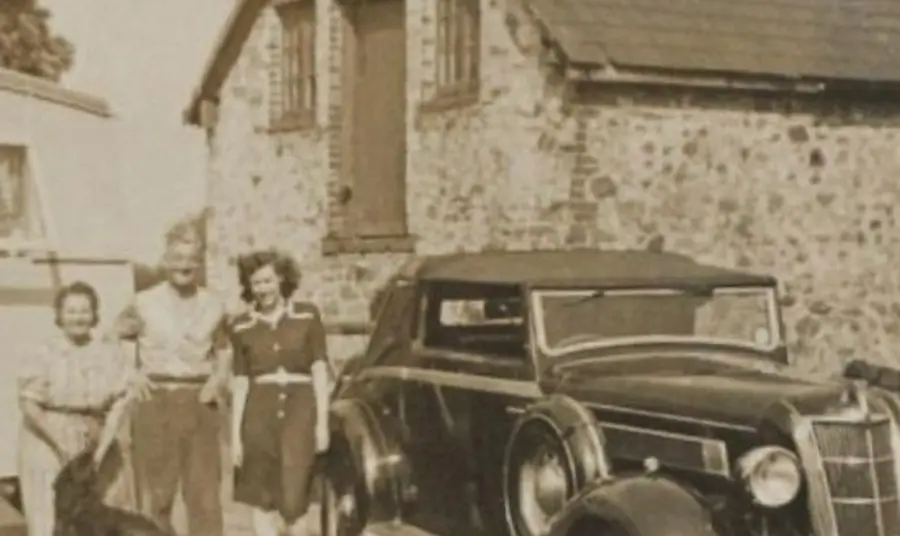 An old photograph showing a car and three people in front of a house