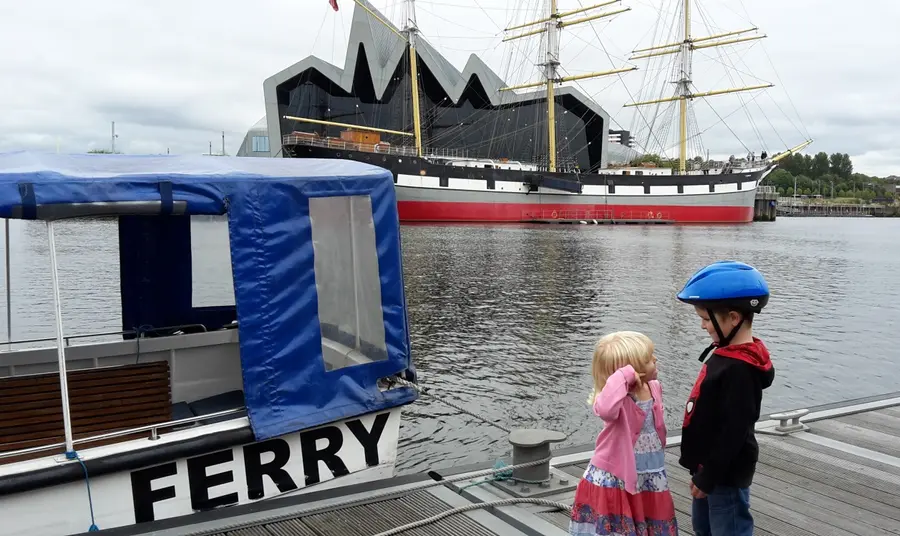 A boy and a girl, stand facing each other on a waterfront near Glasgows Riverside Museum
