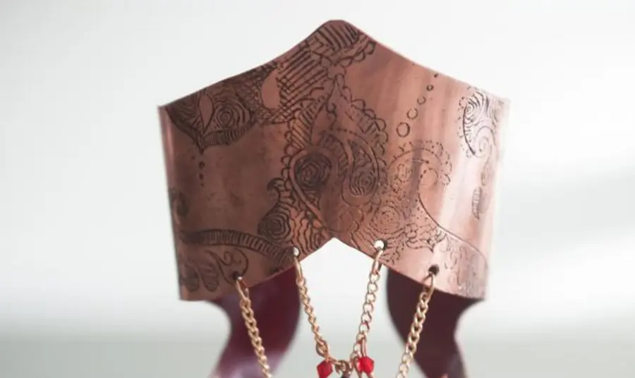 Handmade gold jewellery with red and green gemstones displayed on an intricately carved stand