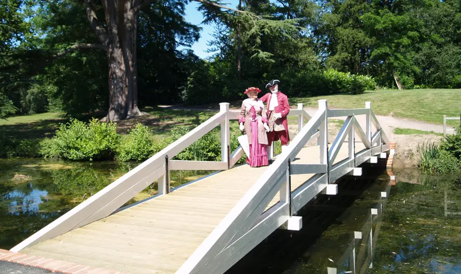 Two people in costume stand on a bridge in Painshill Park