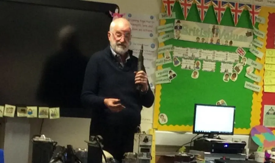 An older man with mining objects talking to a group of school children