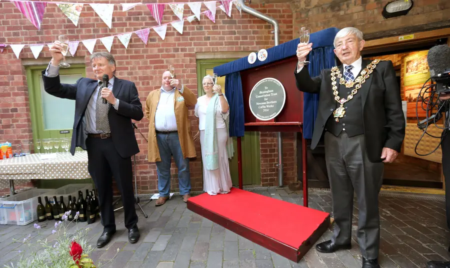 A group of people holding glasses gathered around an unveilled plaque