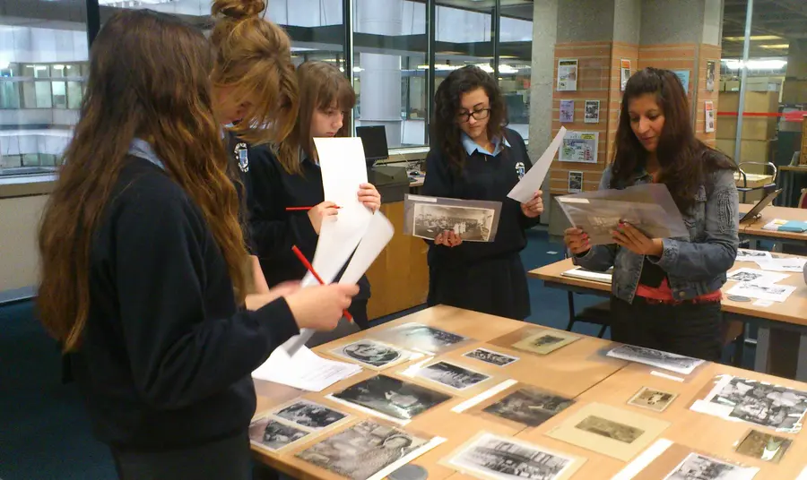 A group of young women standing around a table covered in old photographs