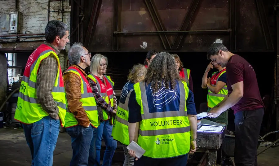 A group of visitors in high vis jackets watch a demonstration from the Master Founder.